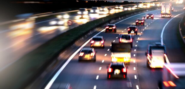 Auf dem Bild ist eine Verkehrssituation mit mehreren Autos auf der Autobahn zu sehen. Alle Autos auf dem teilweise verschwommenen Bild haben ihre Beleuchtung angeschaltet.